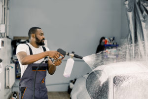 Worker performing a car wash with high pressure water jet and spray foam