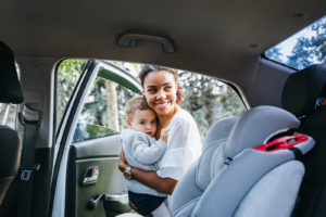 Smiling mother putting baby daughter in a car seat