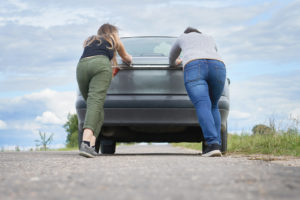two people pushing a car on the road