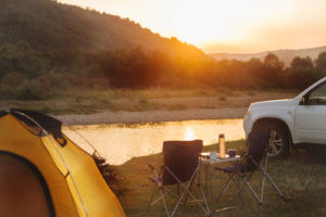 SUV parked next to a yellow camping tent with the view of a river and mountain in the background