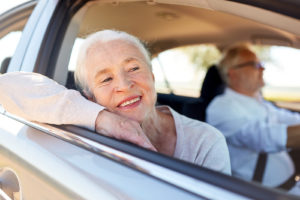 senior woman looking out a car window while a senior male is driving