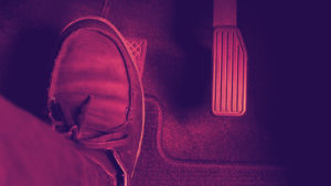 Red tinted picture of a person pressing on the brake pedal of a car