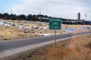 Passing Lane Sign At The Grassy Side Of Road Against Snowy Hill